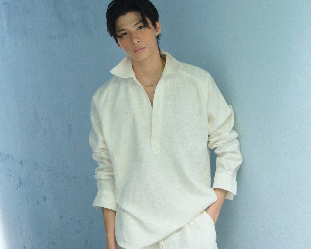 Male person wearing a white linen outfit standing in a narrow passageway with light blue walls in Vietnam.